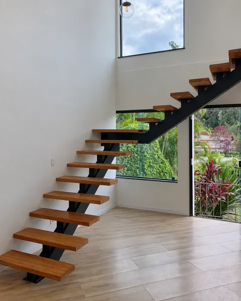 Escada de viga central preta com degraus de madeira em sala de pé-direito duplo com janela para o jardim