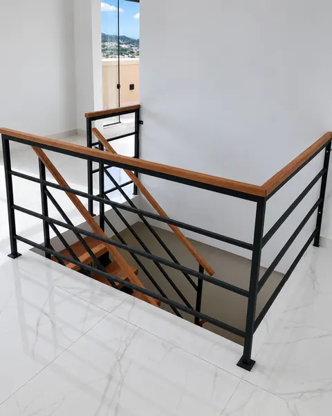 Guarda-corpo de ferro preto com corrimão de madeira contornando o vão da escada, sobre piso de mármore claro