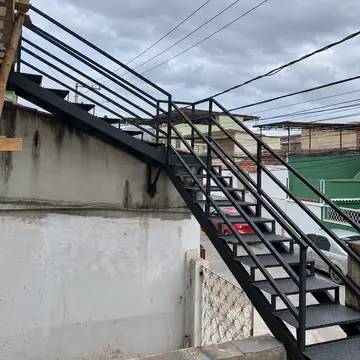 Escada externa toda em ferro preto com degraus de chapa e guarda-corpo, sob céu nublado