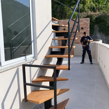 Escada externa de viga central com degraus de madeira e guarda-corpo, em terraço com um instalador ao fundo