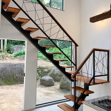 Escada de viga central com guarda-corpo de linhas cruzadas e degraus de madeira, diante de uma janela grande para o jardim